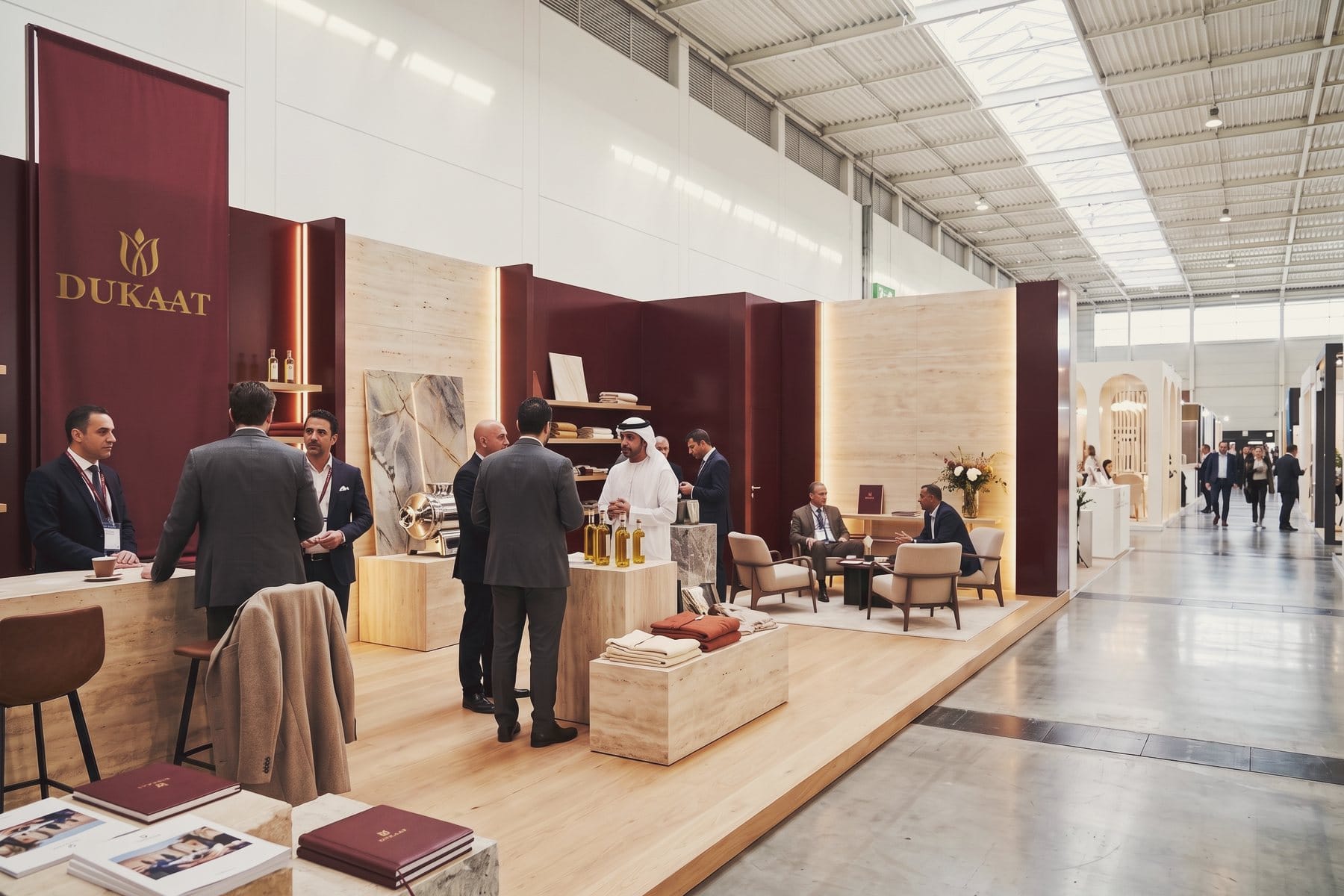 The DUKAAT pavilion at an international trade fair, with products on stone plinths and visitors in conversation.